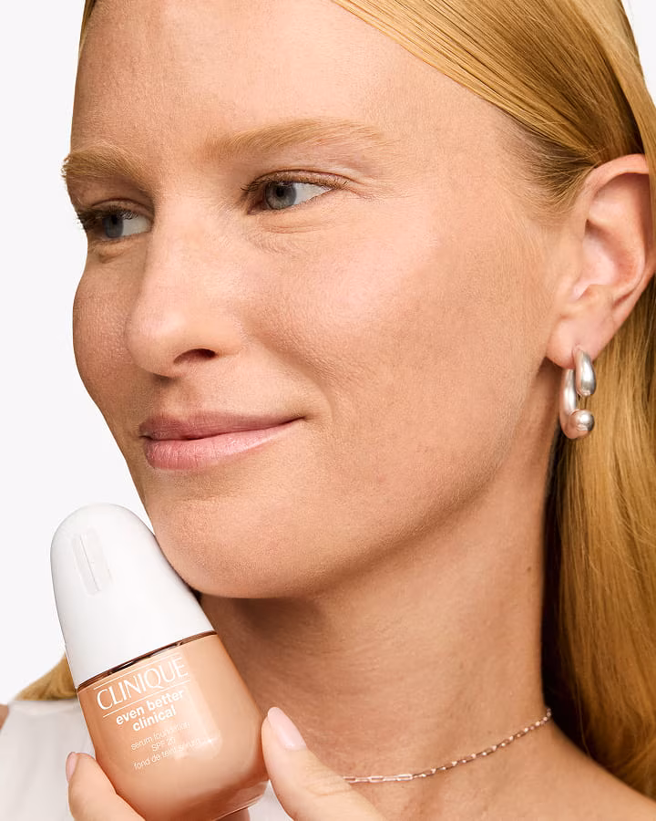 Close up of smiling, bearded man applying Clinique For Men Anti-Age Eye Cream to under eyes, in a bright setting